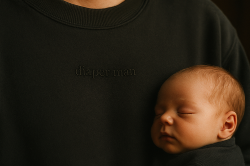 Diaper Man — chest detail, tonal embroidery on black sweatshirt